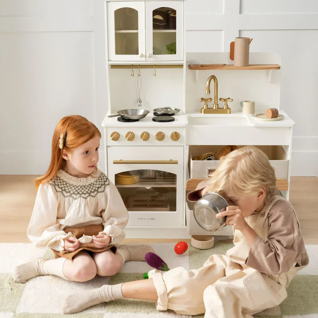 a girl and a boy is sitting on the floor and playing their play food and play kitchen for pretend cooking games