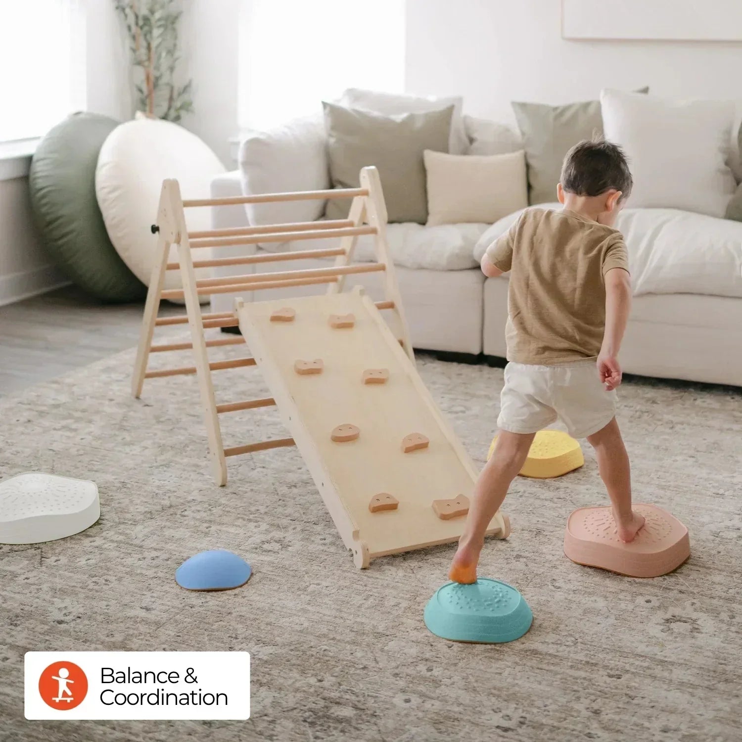 A little boy wearing a khaki short-sleeve shirt and white shorts is playing indoors with Morandi-colored stepping stones and a natural wood climbing frame.