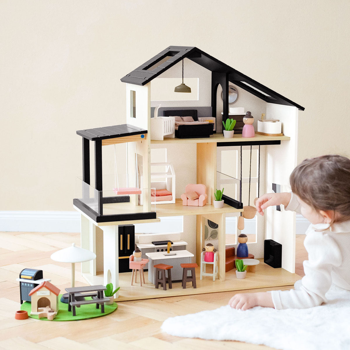 Child playing with the Tiny Land Sweetwood Edge wooden dollhouse and garage, arranging furniture and family figures