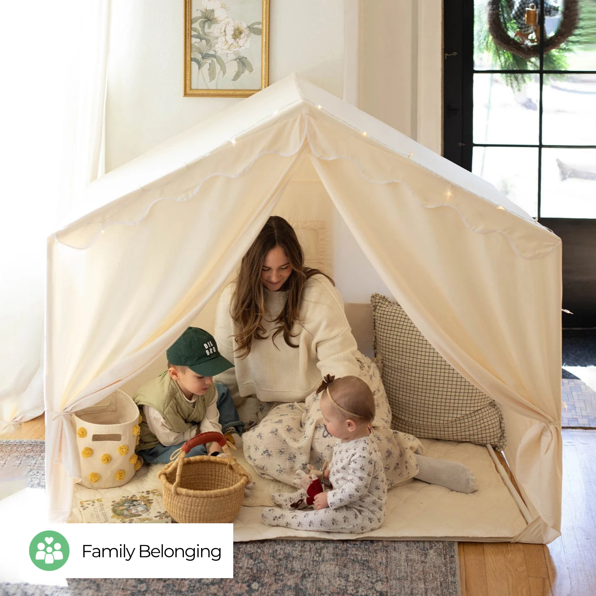 A mother is watching her two kids play inside a white kids play tent at home