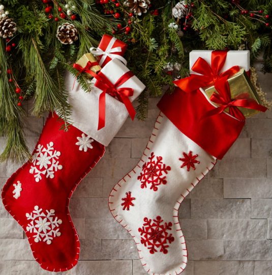 A red Christmas stocking with snowflakes and a white Christmas stocking with snowflakes hang on a fireplace decorated for the holidays.