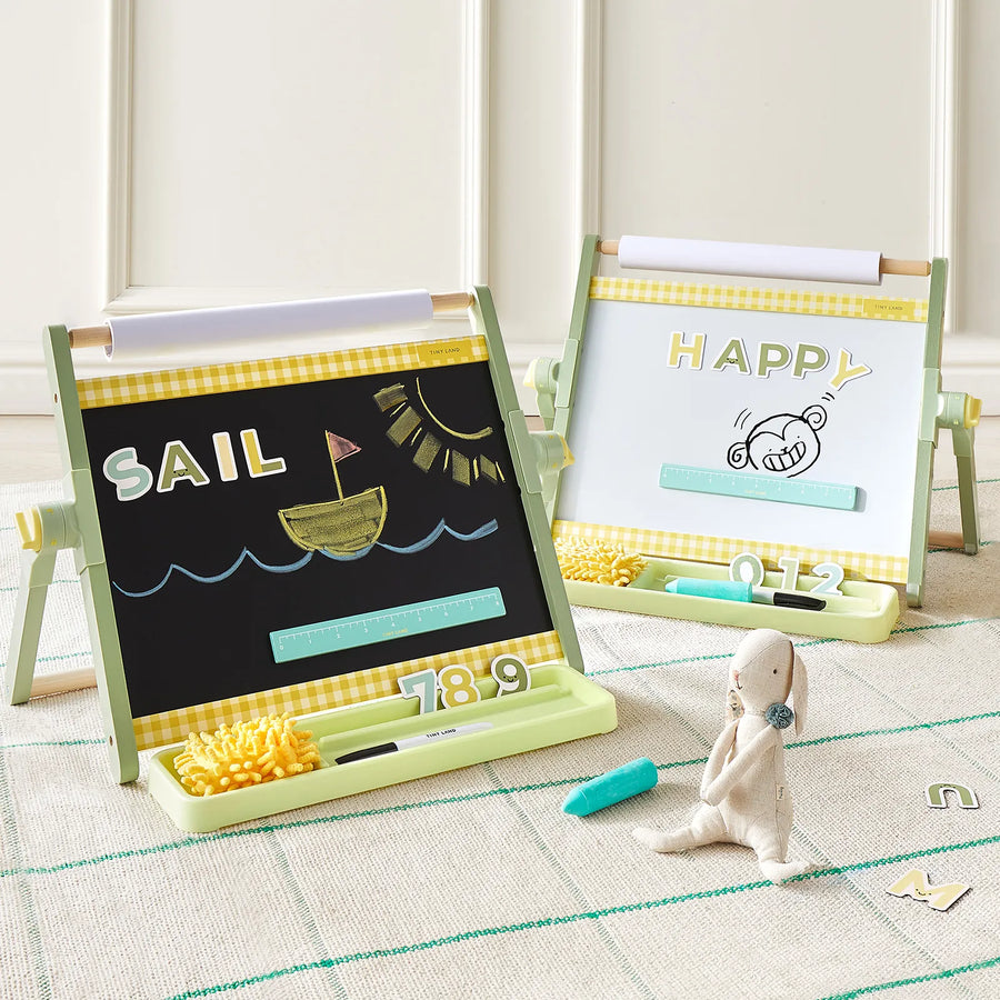 Two light green Tiny LandĀ® Double-Sided Magnetic Tabletop Easels sit on a rug. The left adjustable easel by Tiny Land features a chalkboard displaying "SAIL" with a boat drawing, while the right side offers a magnetic whiteboard showcasing "HAPPY" and a monkey illustration. A plush bunny sits in the foreground next to scattered letters, making this the perfect kidsā art station for creativity and play.|Green