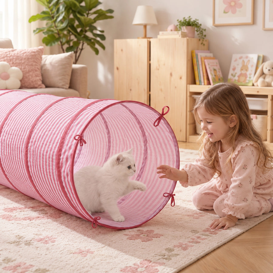 A young girl plays with a white kitten inside a pink and white striped Tiny Land® Adventure Play Tunnel.|Pink