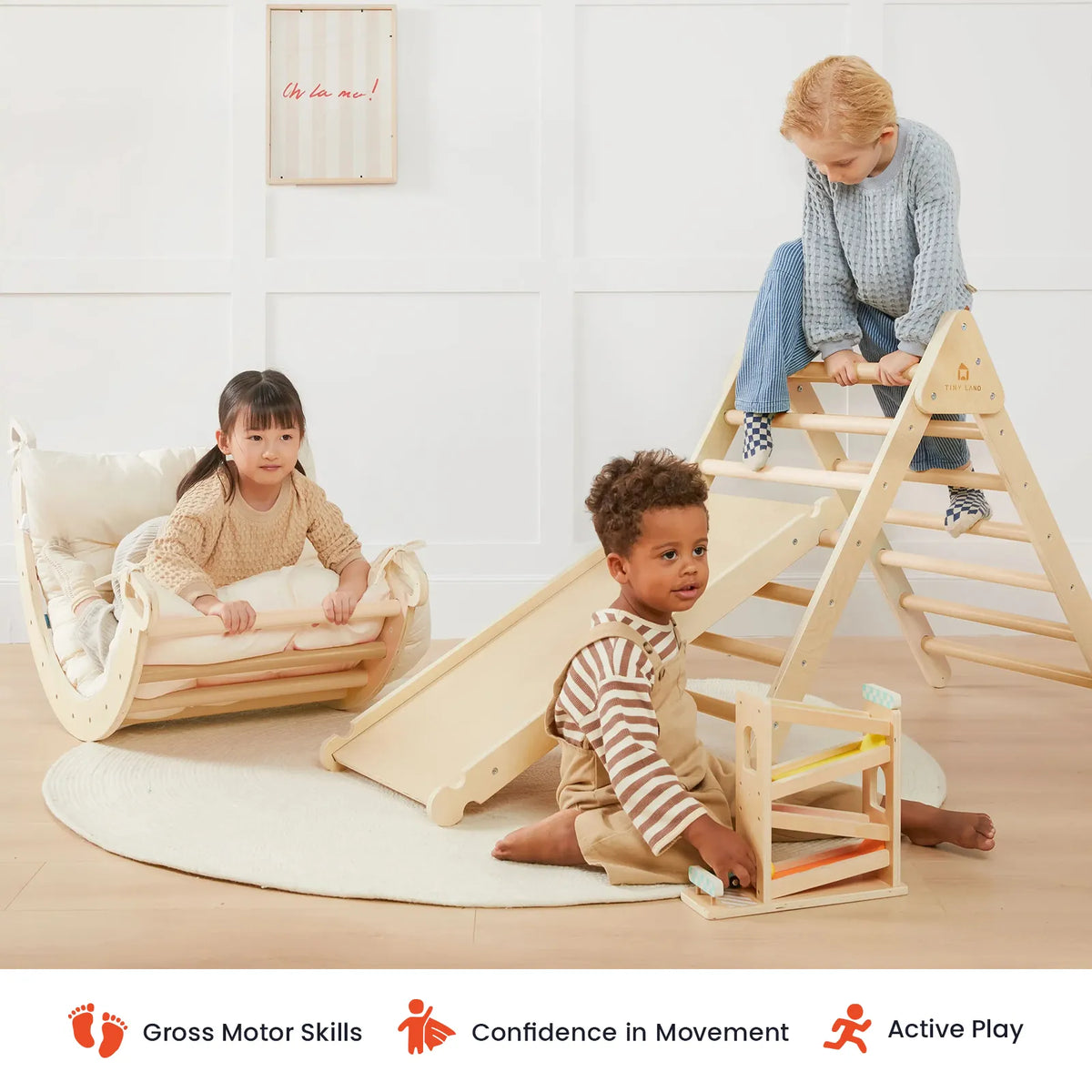 Three young children play indoors with the Tiny Land® 7-in-1 Montessori Climbing Set with Play Pad. One climbs a Pikler triangle from the set, one relaxes in the rocker, and another enjoys a marble run on the padded play cushion. Icons below showcase benefits for gross motor skills, building confidence, and encouraging active play.