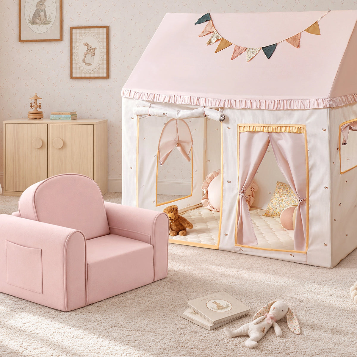 A pink Tiny Land® Cozy Nook – GentleSnug Chair & Playhouse Tent sits beside a playhouse tent decorated with fabric bunting, creating a cozy kids reading nook.|Pink