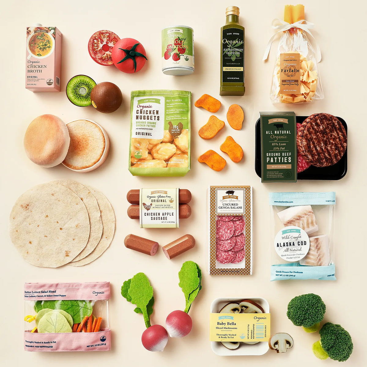The Tiny Land® Complete Cooking Play Food Set by Tiny Land features an assortment of neatly arranged organic-inspired groceries—including veggies, meats, bread, tortillas, oil, cheese, and sauces—artfully displayed on a cream surface to resemble a delightful kitchen play set that’s perfect for hours of pretend play food fun.