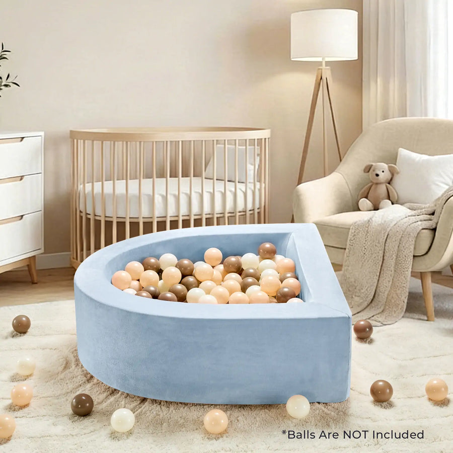 A Tiny Land® PlayNest Soft Foam Ball Pit (balls not included) in blue, designed for sensory play, sits in a cozy nursery filled with pastel balls and surrounded by a crib, dresser, armchair, floor lamp, and teddy bear. Text reads: “*Balls are NOT Included.”.|Blue