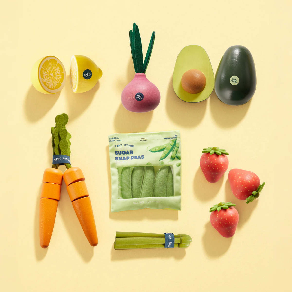 The Tiny Land® Organic Fruit & Veggie Pack by Tiny Land INC features wooden fruits and vegetables like lemon, beet, avocado, carrots, snap peas, strawberries, and celery arranged on a pale yellow background for realistic play.