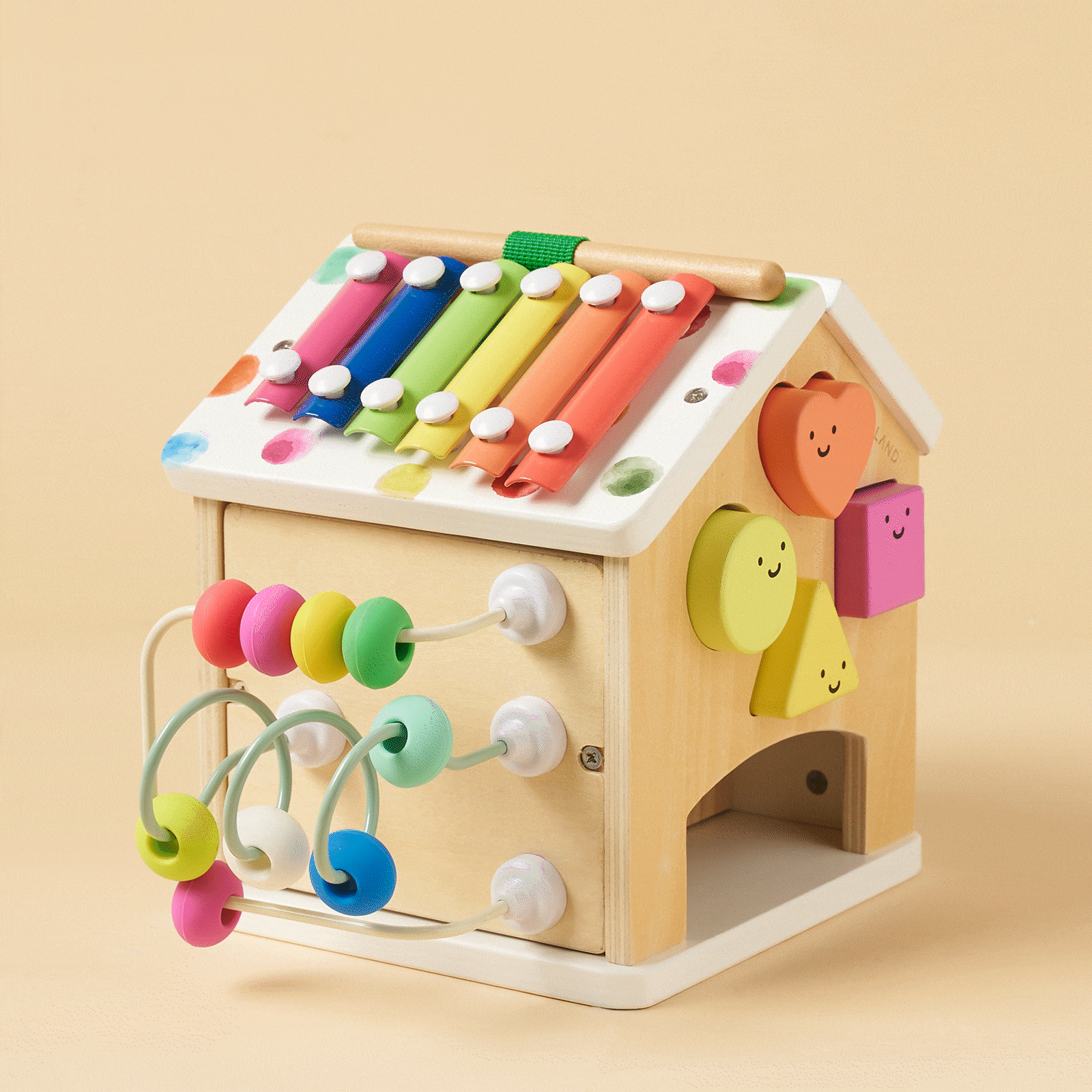 The Tiny Land® Cottage Activity Cube - Rainbow by Tiny Land is a house-shaped Montessori toy with a xylophone, bead wires, and smiling shape blocks on a light beige background—perfect for engaging, colorful developmental play.