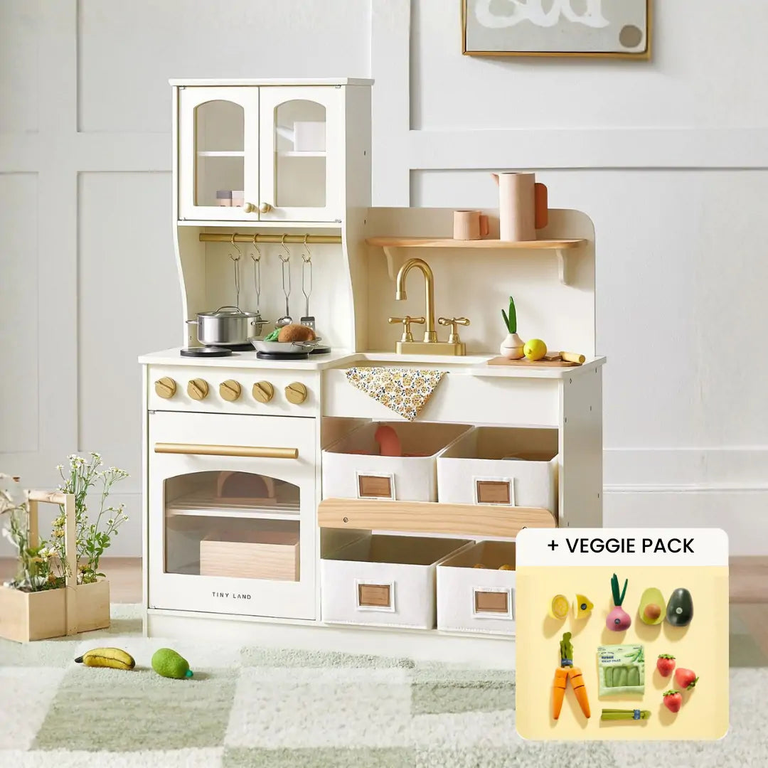 The Tiny Land® Smart Storage Kitchen Harvest Set by Tiny Land is shown in a cozy room, featuring an oven, sink, cupboards, shelves, and storage bins. Inset: veggie pack play food with toy carrots, tomato, and corn for pretend play fun.