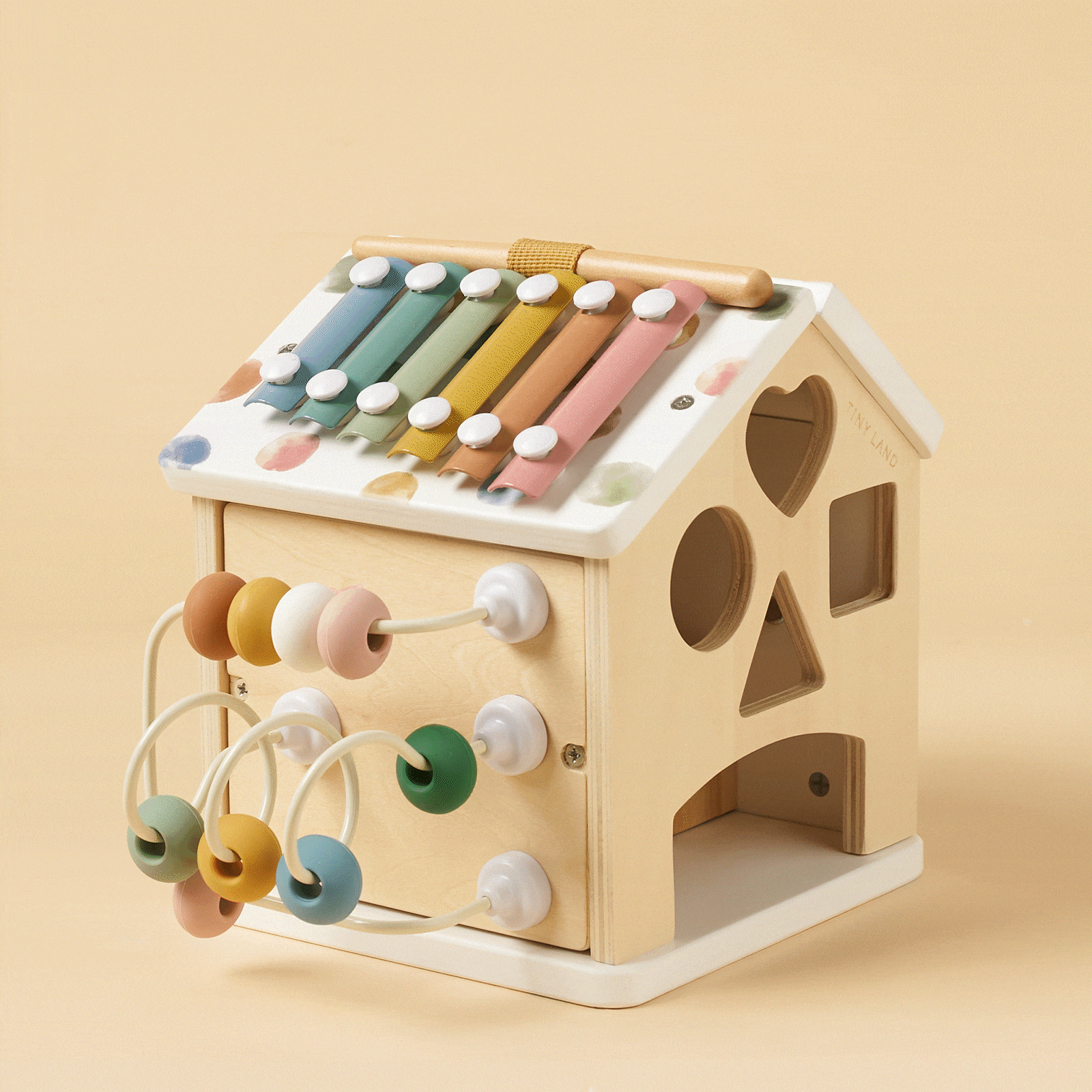 The Tiny Land® Cottage Activity Cube - Morandi by Tiny Land is a wooden, house-shaped Montessori toy with a colorful xylophone roof, bead maze, and shape sorter—an engaging developmental set placed against a beige background.