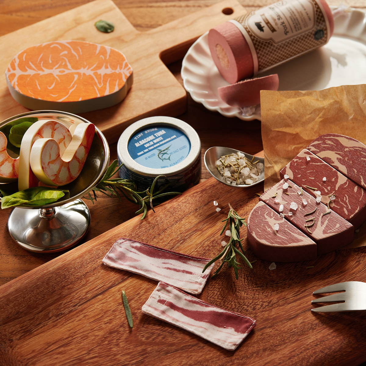 The Tiny Land® Organic Meat & Seafood Pack features realistic paper steak, bacon, shrimp, and cheese arranged with herbs and salt on wooden boards, offering children a fun charcuterie board pretend play experience.
