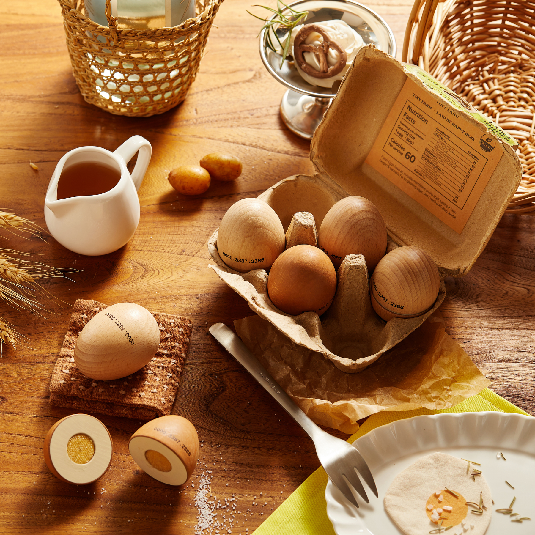A carton of brown eggs from the Tiny Land® Egg Combo Playset by Tiny Land INC sits on a wooden table, with a broken egg revealing a yellow yolk—ideal for play kitchen scenes with wicker baskets, a jug, and plate for added realism.
