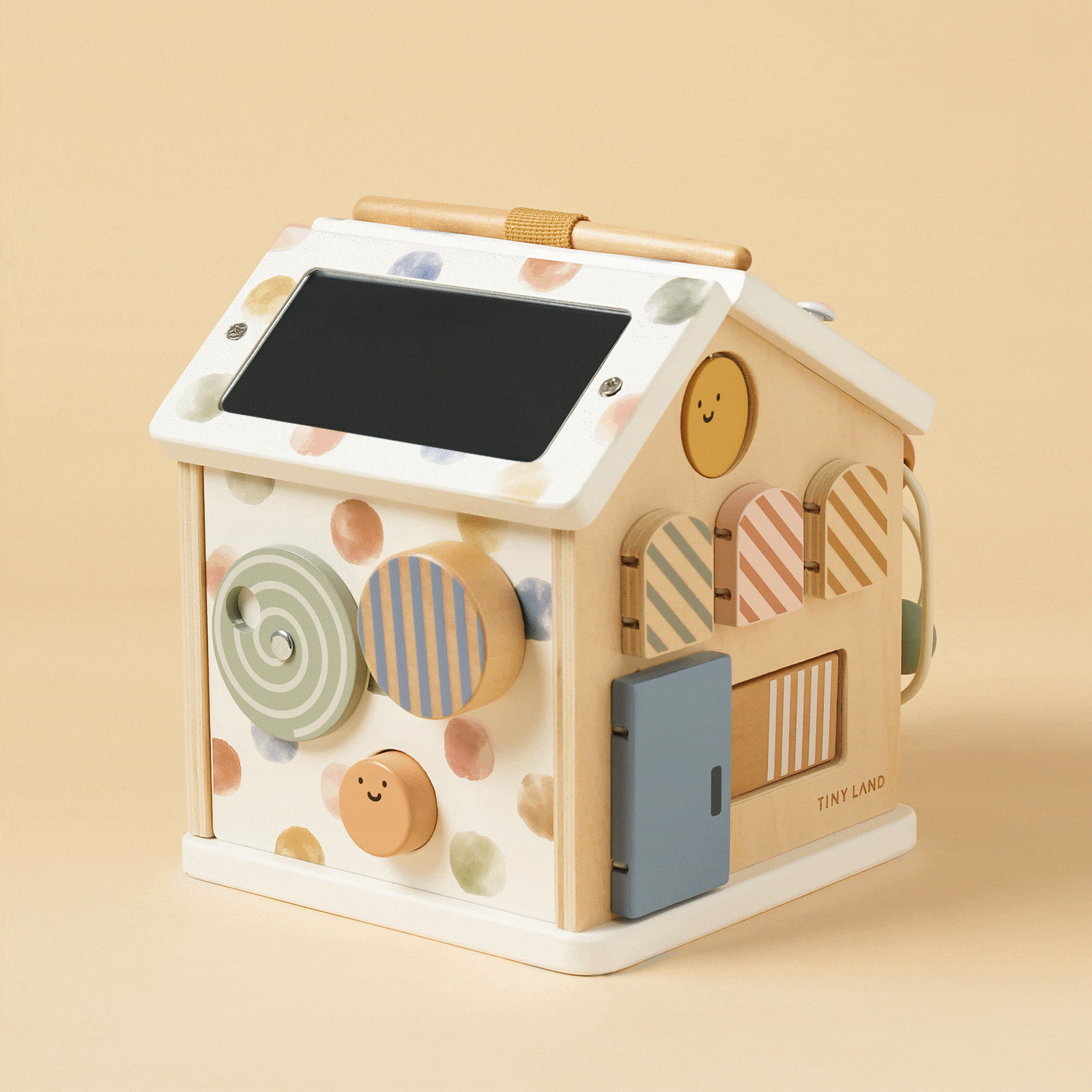 The Tiny Land® Cottage Activity Cube - Morandi by Tiny Land is a pastel house-shaped Montessori toy featuring a solar panel roof, polka dots, spinning circles, smiley faces, and a blue door—perfect for developmental play on a beige background.
