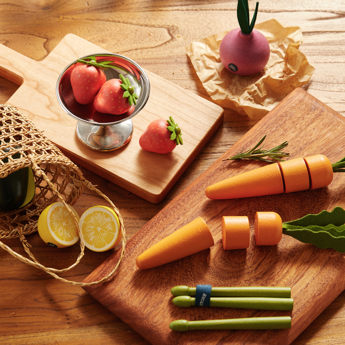 The Tiny Land® Organic Play Food - 4 Sets by Tiny Land features wooden strawberries, carrots, lemon, and radish on boards with a net bag and green tongs—ideal pretend food toys for imaginative play.
