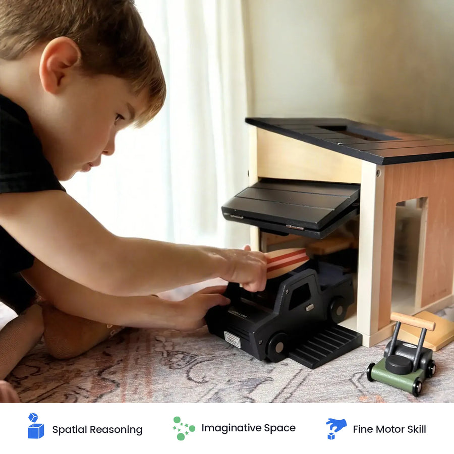 A young child plays with the Tiny Land® Wooden Dollhouse - Garage from Tiny Land, using the included toy truck and loading dock while focusing intently. Icons below highlight benefits such as spatial reasoning, imaginative play, and fine motor skill development—making it perfect for kids’ pretend play.