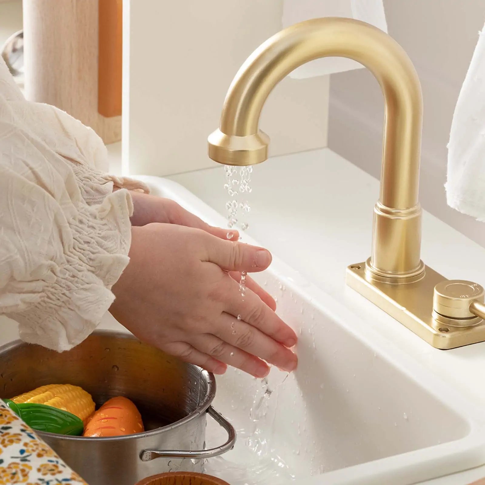 A child washes their hands under the running water of the Tiny Land® Play Kitchen with Cream Iconic Aqua faucet, while toy veggies in a pot nearby inspire imaginative pretend play by Tiny Land.
