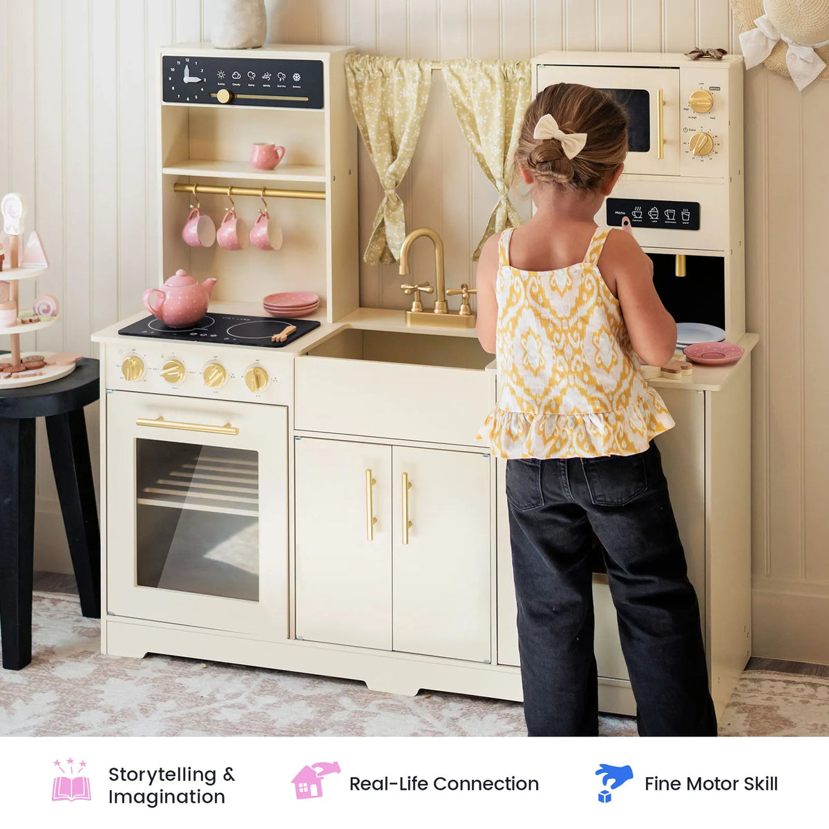 A young child enjoys imaginative play with the Tiny Land® Iconic Wooden Play Kitchen – Cream Pretend Cooking Set for Kids, pretending to cook alongside pink tea sets and utensils. Icons below showcase benefits such as storytelling, real-life connection, and fine motor skill development.