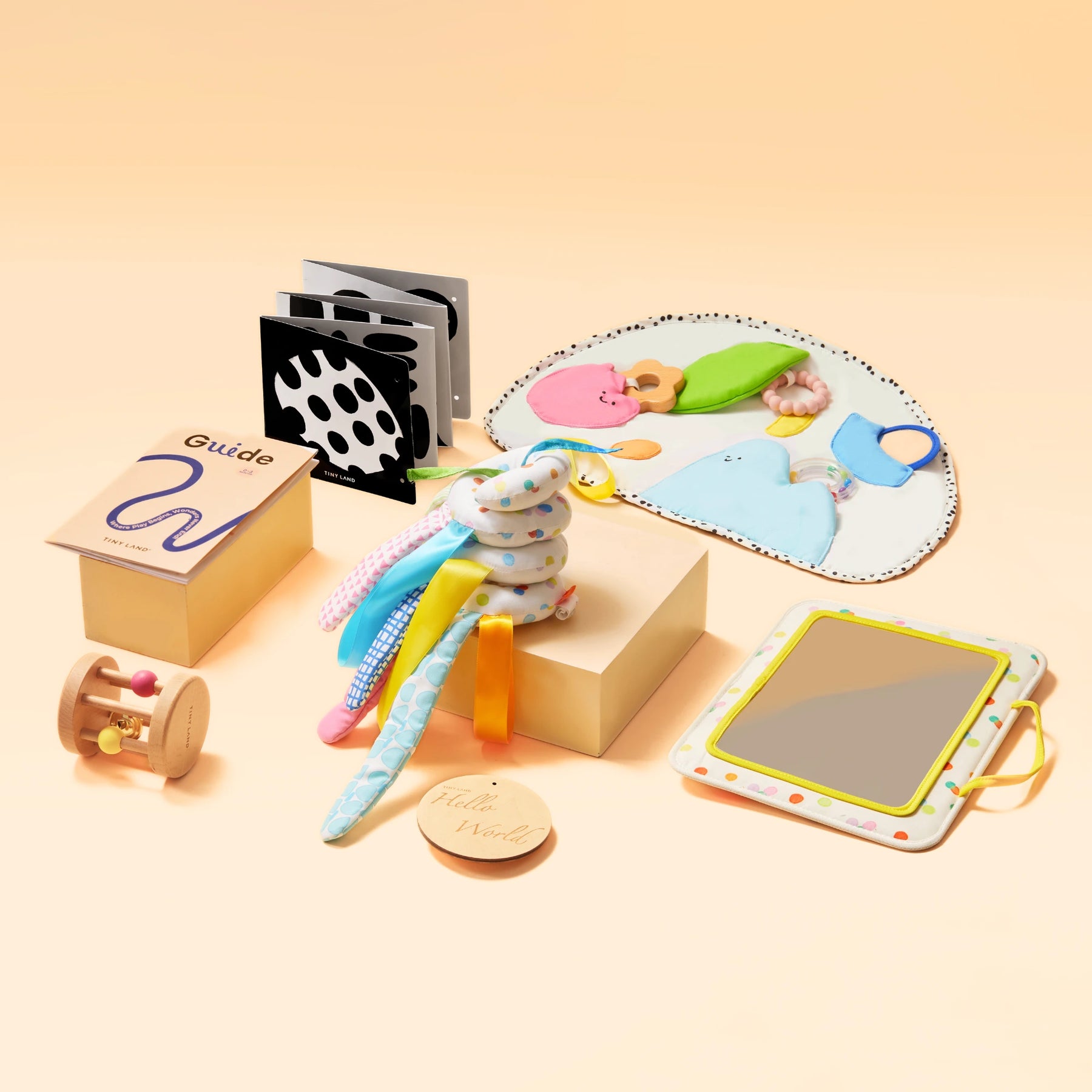 Tiny Land® Montessori Toys for Newborns (0–3 Months) by Tiny Land Official Store features a colorful set with tummy time playmat, wooden rattle, fabric spiral toy, mirror, black-and-white cards, and guide booklet on a peach background.