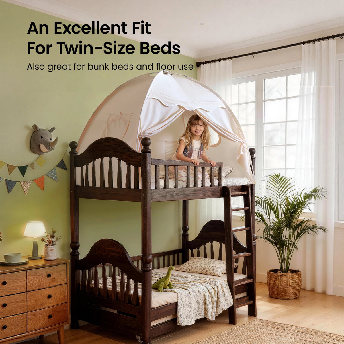 A girl sits atop a dark wood bunk bed fitted with a Tiny Land® Kids Bed Tent by Tiny Land. The cozy kids' room, featuring plants, animal wall art, and natural light, highlights this tent's perfect fit for twin-size beds and playful hideaways.|Beige