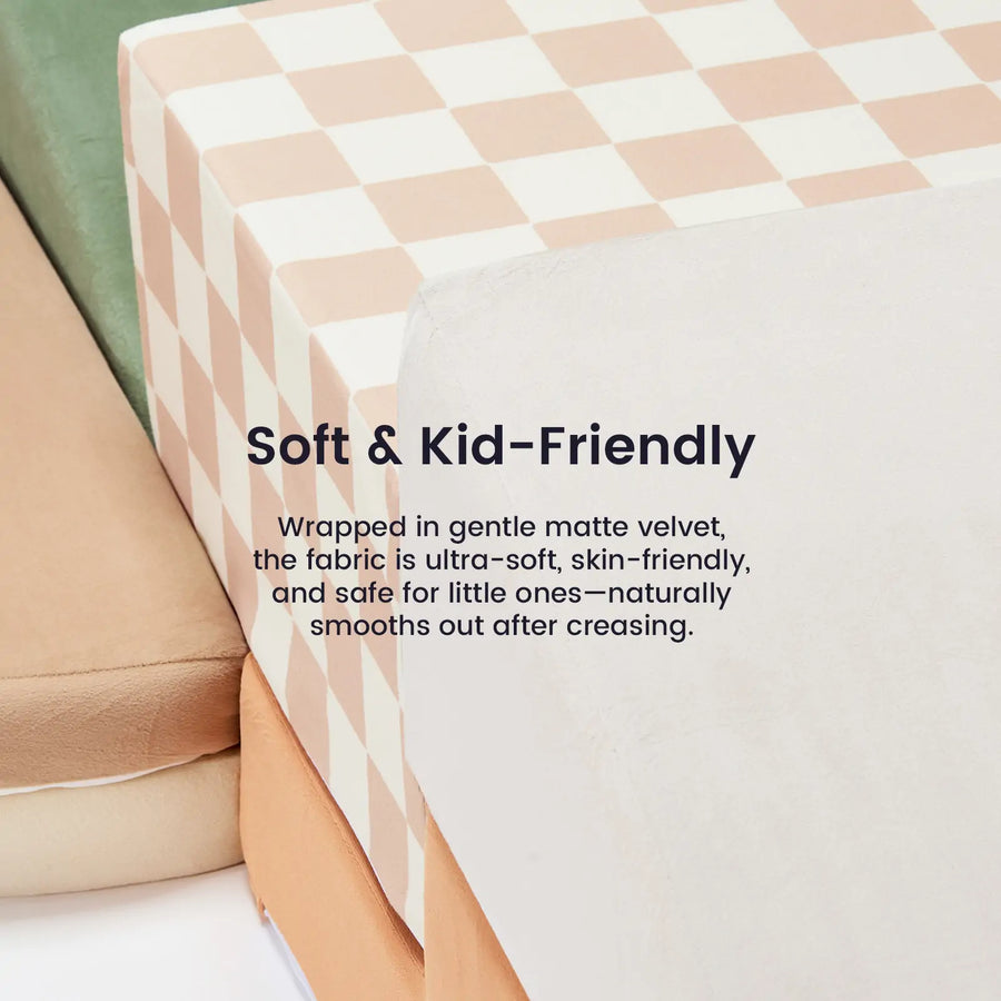 A close-up of three stacked Tiny Land® PlayNest Climbing Blocks, each with different covers including a peach and white checkerboard. Ultra-soft matte velvet from Tiny Land is skin-friendly—perfect for safe, kid-friendly comfort, just like a foam play set.