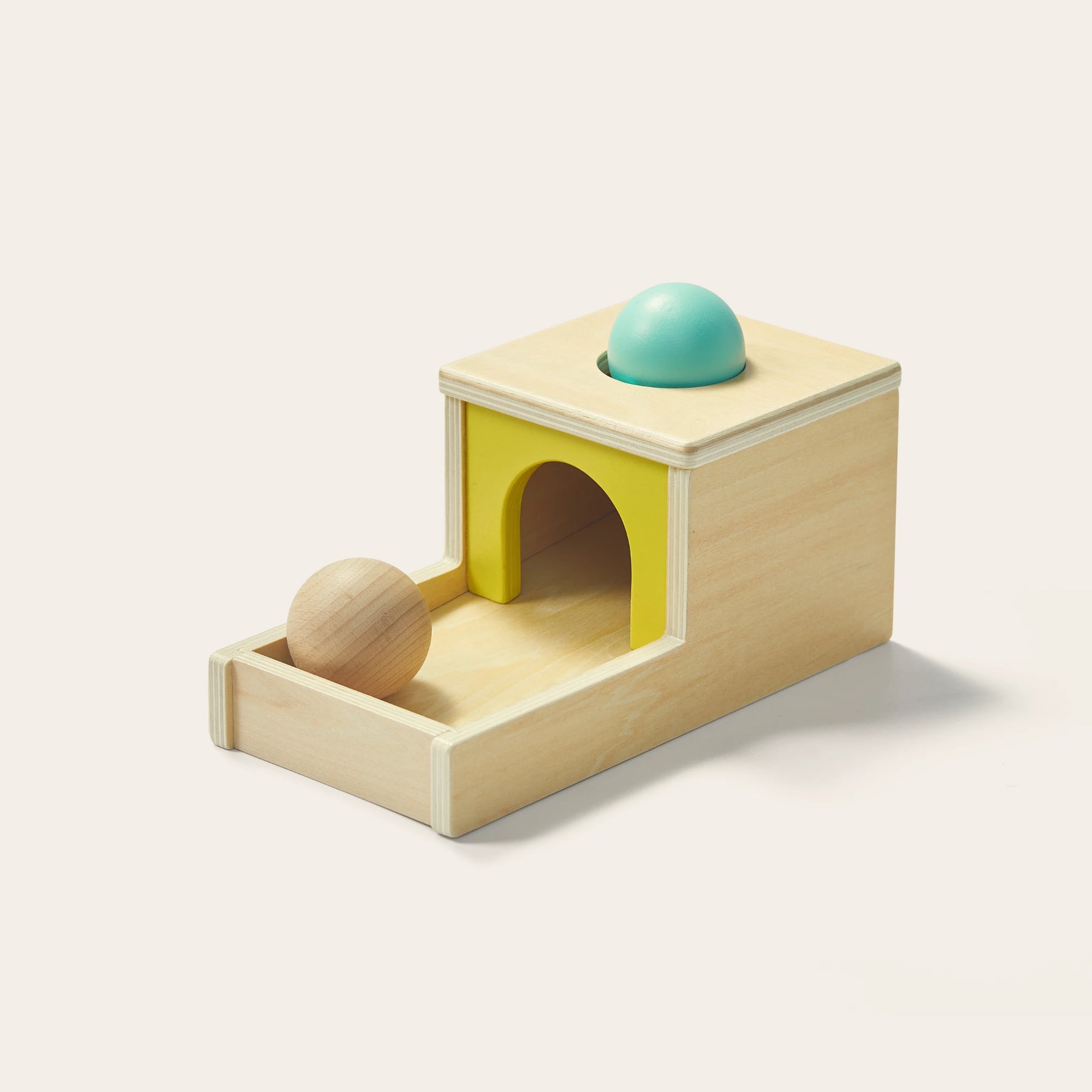 The Tiny Land® Montessori Toys for Newborns (7–9 Months) by Tiny Land features a wooden ramp, yellow arch, and sensory ball that rolls through a hole into a tray, encouraging hands-on exploration and inspired by the Object Permanence Box.