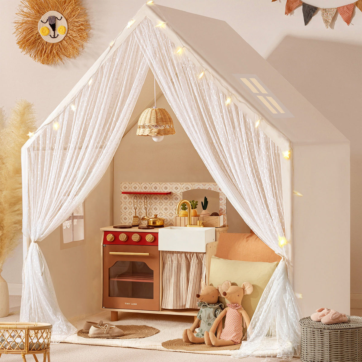 The Tiny Land® Chef’s Corner Playset – Cream Playhouse + Mediterranean Kitchen Set features a neutral decor with sheer curtains, soft lighting, plush toys, a woven wall hanging, and dried pampas grass for natural accents.