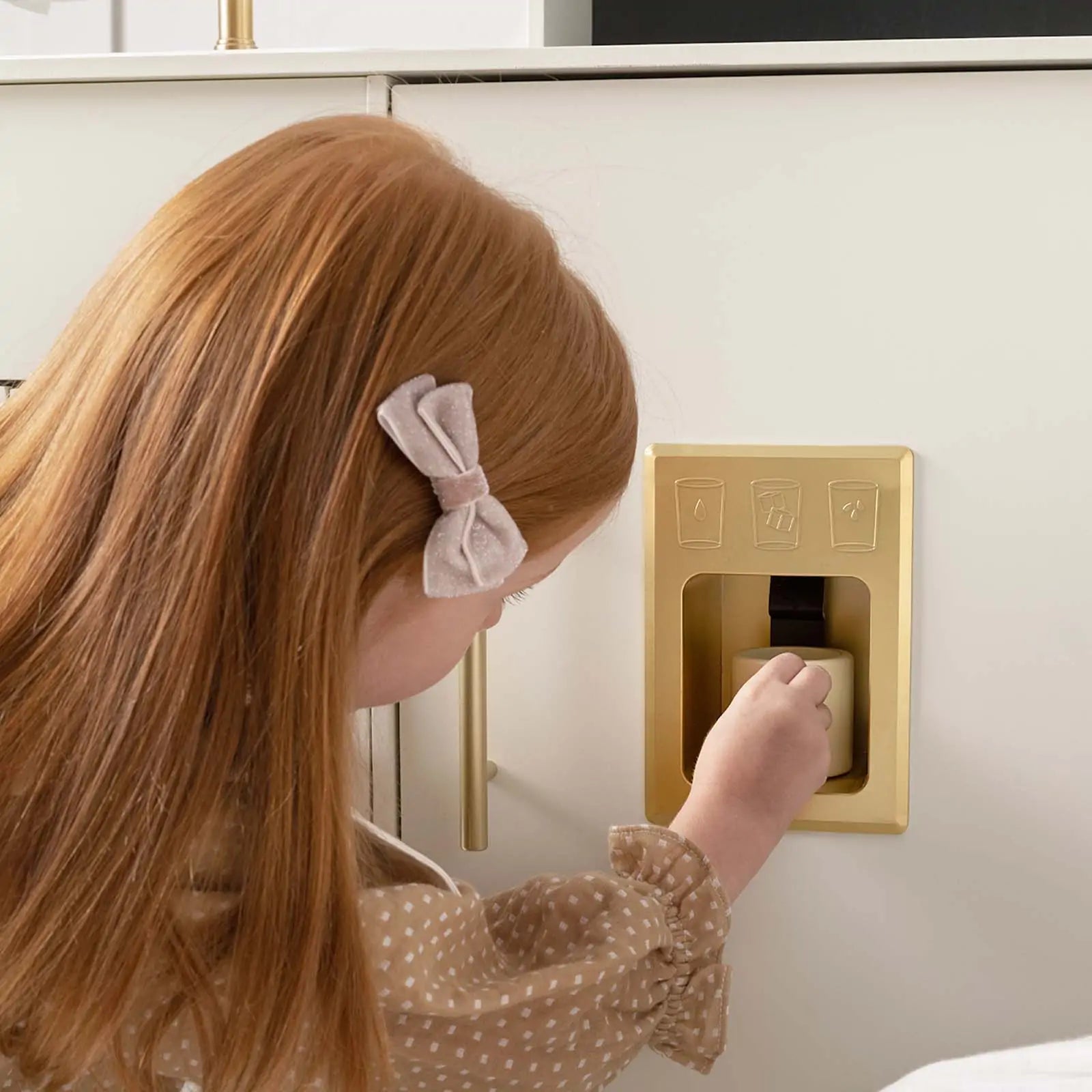 A red-haired girl with a bow enjoys pretend play with the Tiny Land® Play Kitchen with Running Water—Iconic Aqua Kitchen in Cream by Tiny Land.