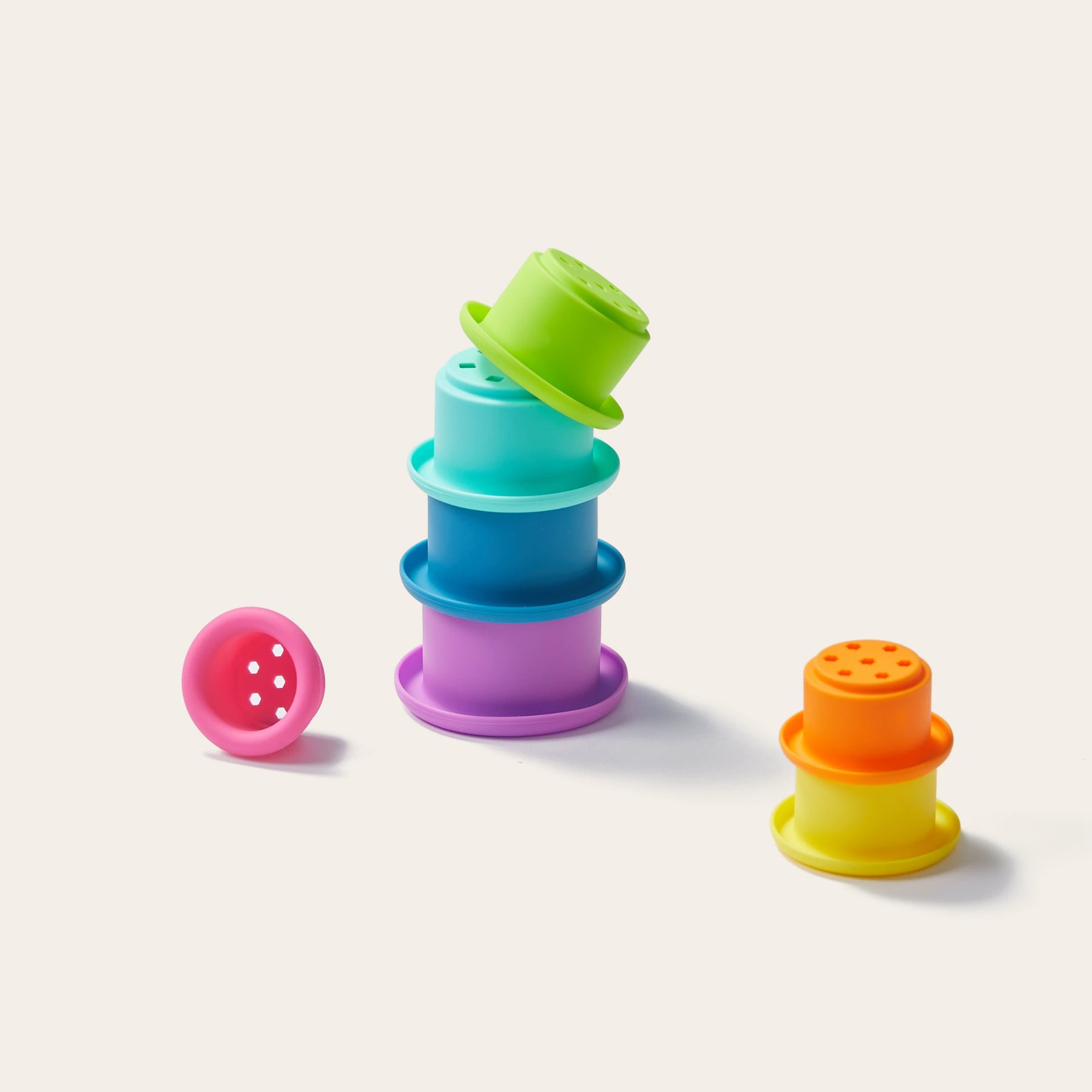 The Tiny Land® Montessori Toys for Newborns (7–9 Months) by Tiny Land feature colorful plastic stacking cups. On a plain off-white background, a green cup tops the stack, a pink cup lies sideways, and an orange-yellow cup stands alone.