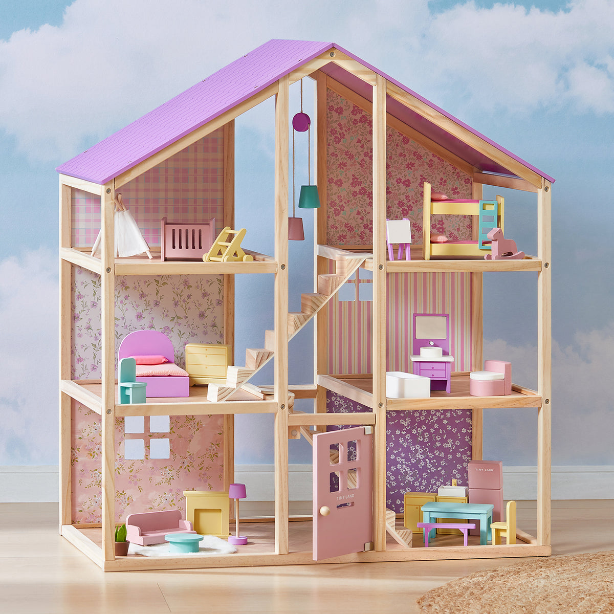 The Tiny Land® Sweetwood Dollhouse without Dolls by Tiny Land features an open front, pink and purple roof, floral wallpaper, and wooden furniture—perfect for girls. The background shows a sky with clouds for added charm.|Unicorn