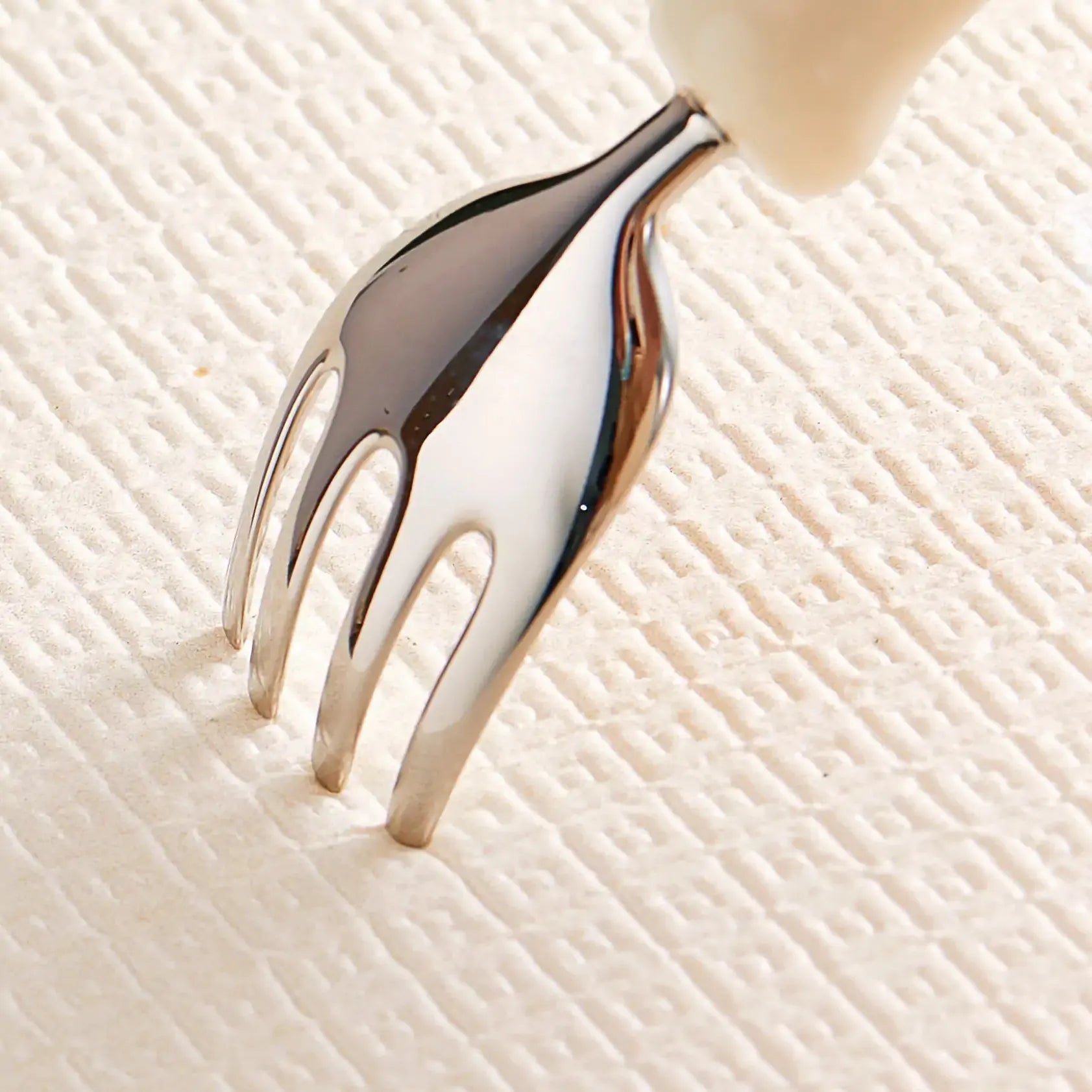 A silver fork with a white handle rests on the textured surface of the Tiny Land® Double-Sided Baby Playmat Forest Track Wonder by Tiny Land, highlighting the playmat’s stylish and practical off-white, waterproof design.