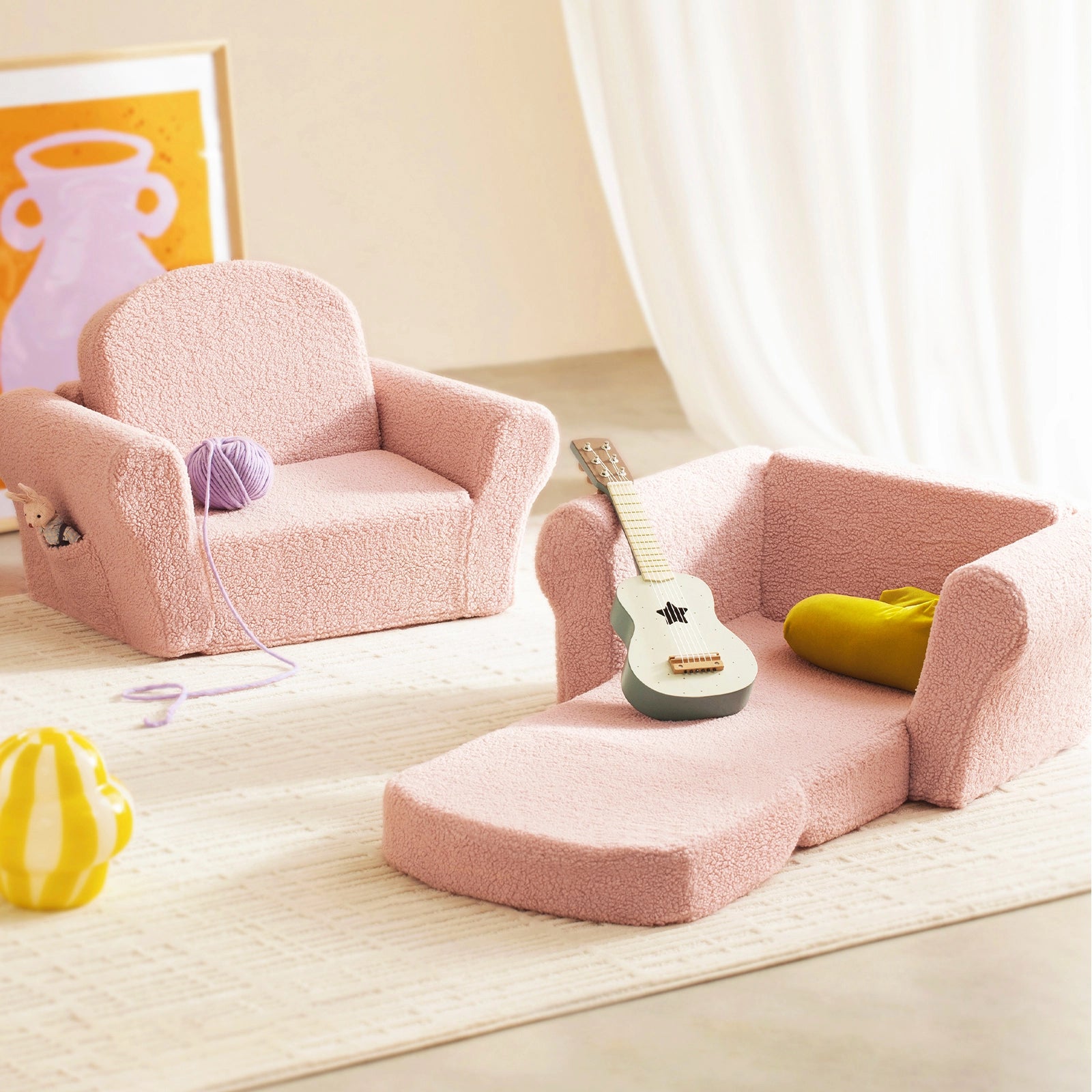 Two Tiny Land® Afternoon Couch - Pink Kids Chairs by Tiny Land are shown; one unfolds into a lounge with a small guitar and yellow pillow. A purple yarn ball and framed pink art brighten the room, perfect for play or rest.