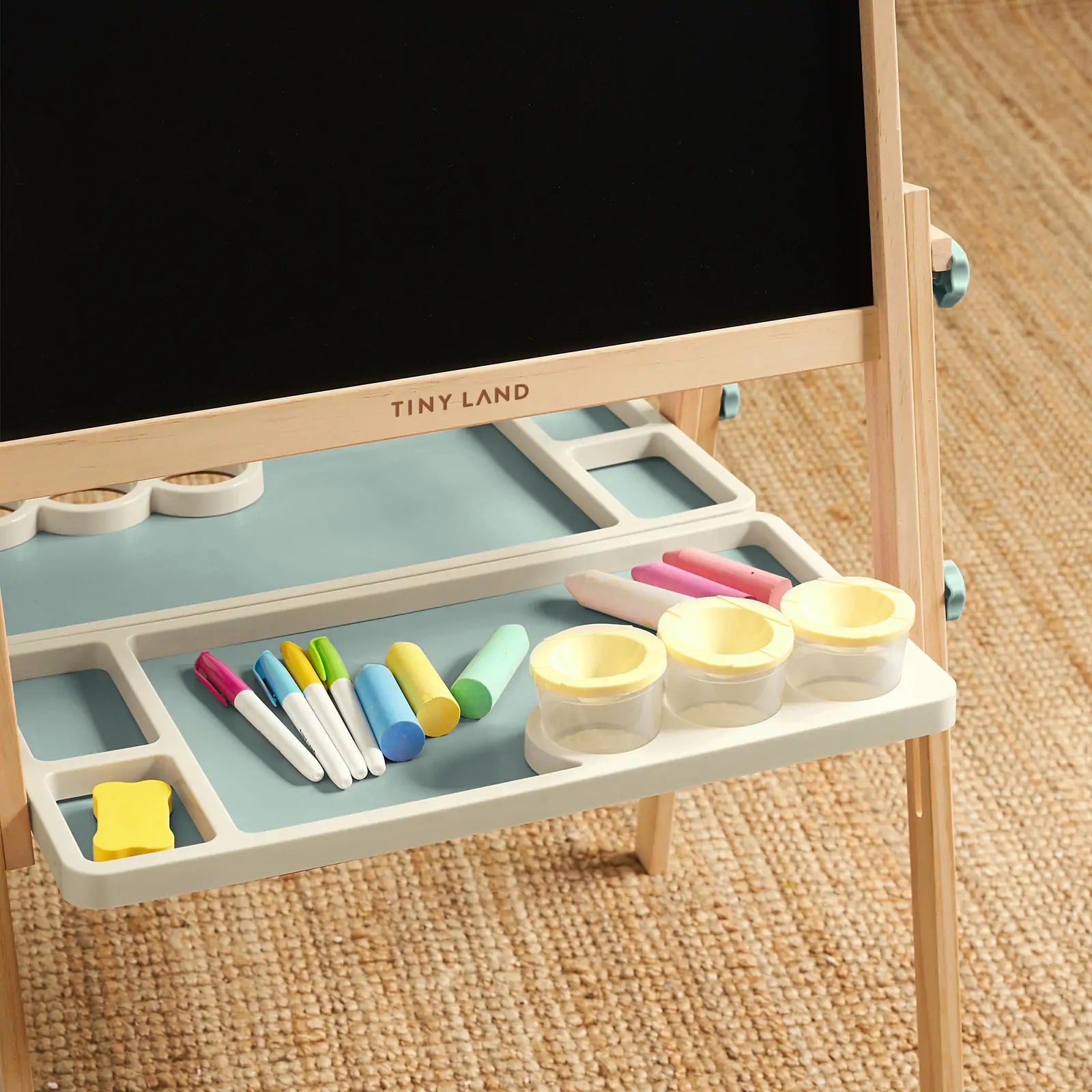 The Tiny Land® Magnitales Easel for Kids - Green features a blackboard, erasers, chalk, transparent cups with yellow lids, assorted markers, and chalk sticks on a tray shelf—an adjustable art easel by Tiny Land for creative play.