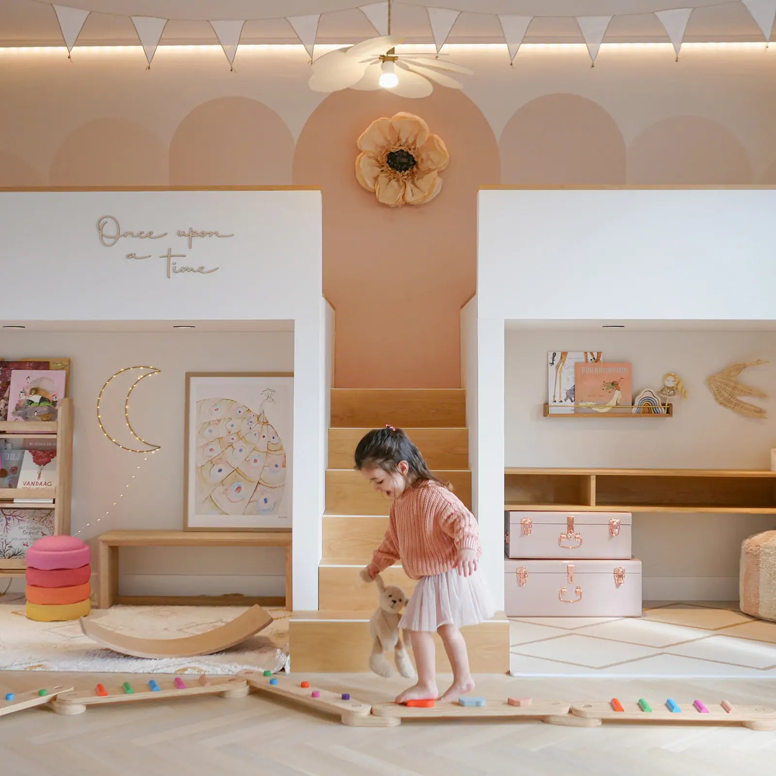 A young girl walks barefoot on the Tiny Land® Balance Beam by Tiny Land, holding a stuffed animal in a pastel children’s playroom with bunk beds, playful decor, and soft lighting.
