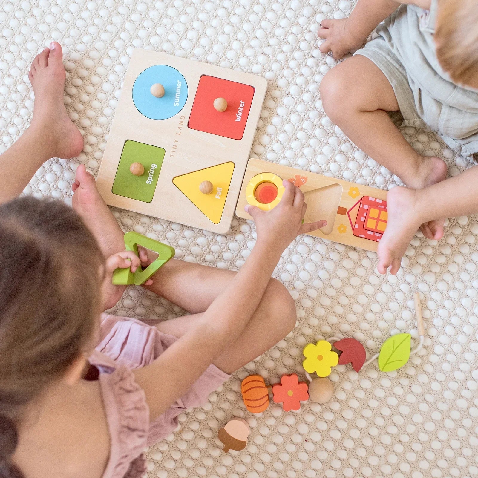 Two children play on a textured rug with the Tiny Land® Montessori Toys for Toddlers (18–24 Months), exploring colorful wooden puzzles with shapes, seasons, and nature-themed pieces like flowers and leaves from Tiny Land.
