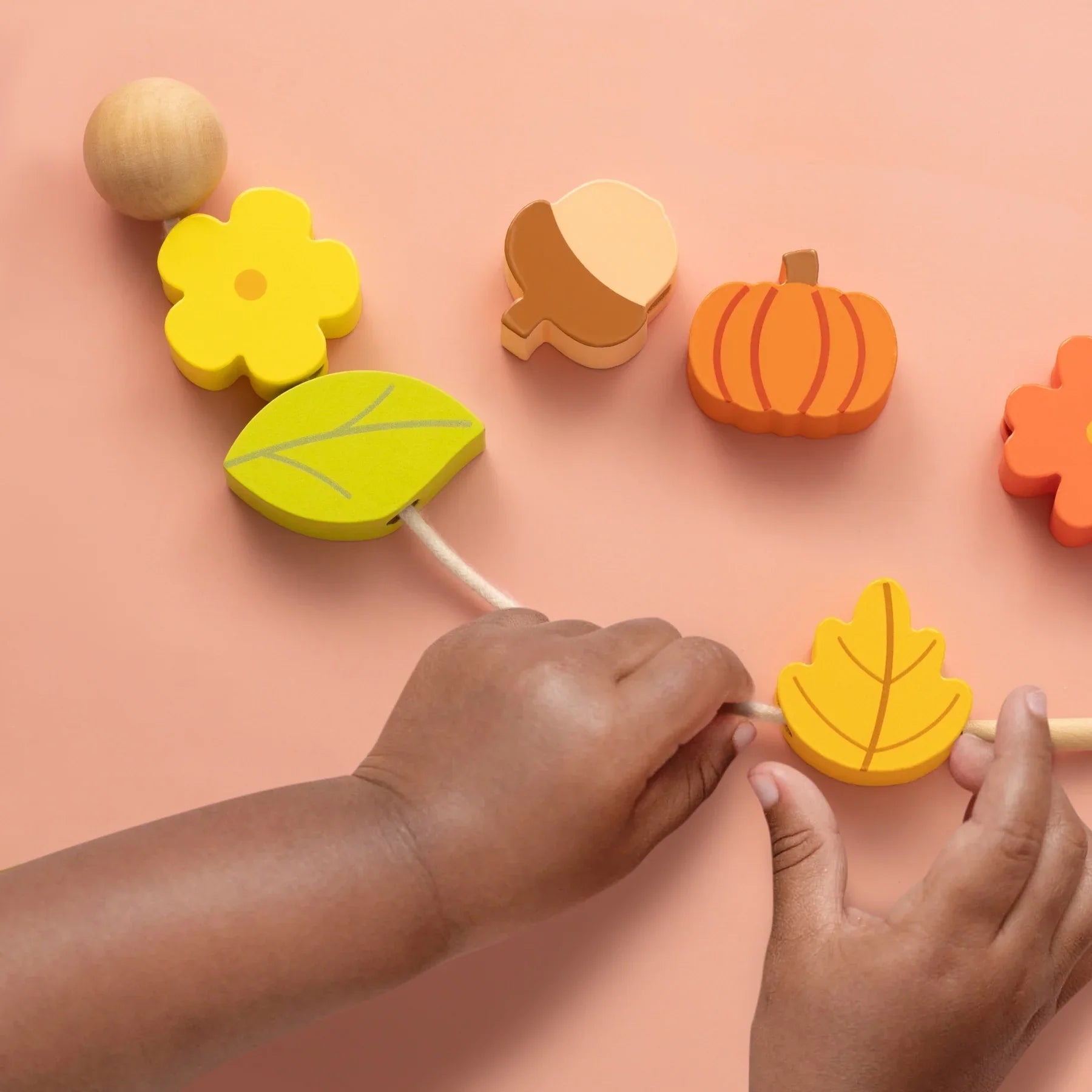 A child threads a string through colorful leaf, flower, acorn, and pumpkin beads from the Tiny Land® Montessori Toys for Toddlers (18–24 Months)—a hands-on learning toy by Tiny Land designed for interactive play.