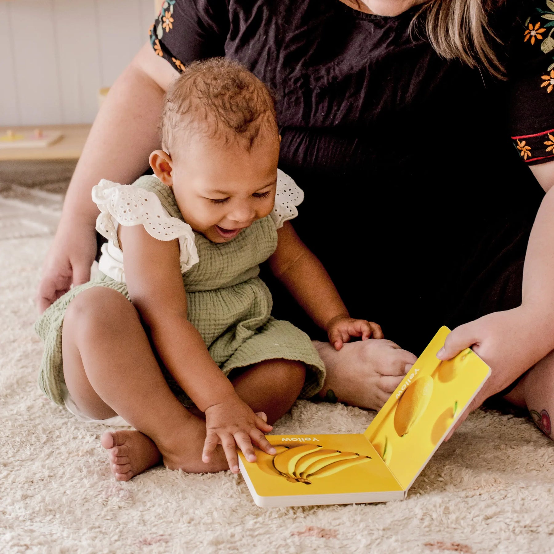 A smiling baby (13–15 months) sits with an adult, happily exploring a colorful book about bananas—engaged together like theyre using the Tiny Land® Montessori Toys for Toddlers from Tiny Land.