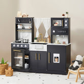 The Tiny Land® Iconic Wooden Play Kitchen – Black, by Tiny Land, features a stove, oven, sink, microwave, shelves, toy pots, dishes, utensils on the counter, plus play accessories. A stuffed animal and storage bins sit nearby on the floor.
