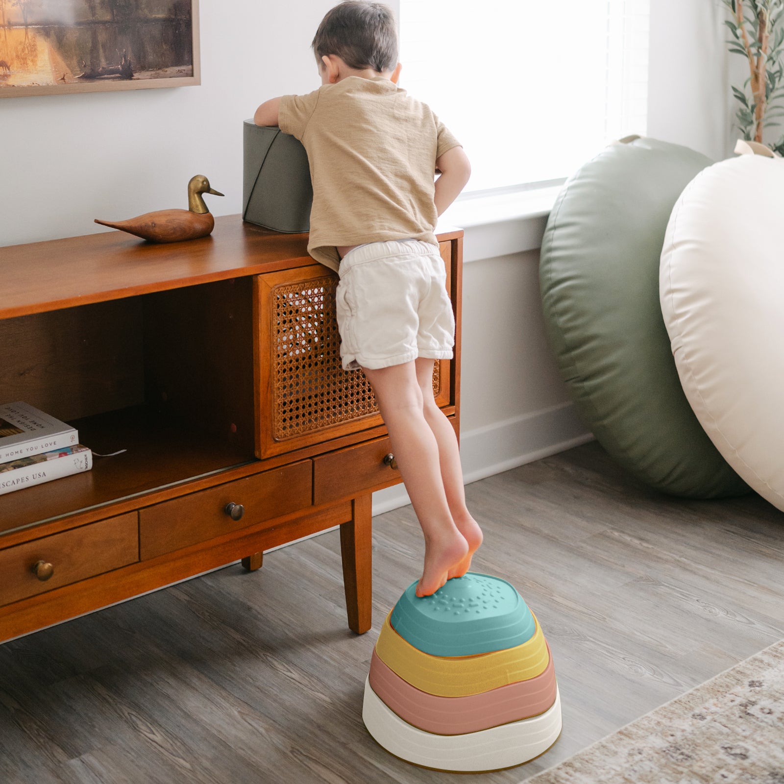 A young child stands on Tiny Land® Stepping Stones - Beach Vacation by Tiny Land, reaching for an object on a console table in a bright living room—ideal for building motor skills through this fun obstacle course.