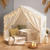The Tiny Land® Kids Tent – Large Cozy Tent with Star Lights by Tiny Land features soft pillows, a blanket, and a small sofa on a woven rug, creating a warm, inviting atmosphere perfect for kids to play and relax.