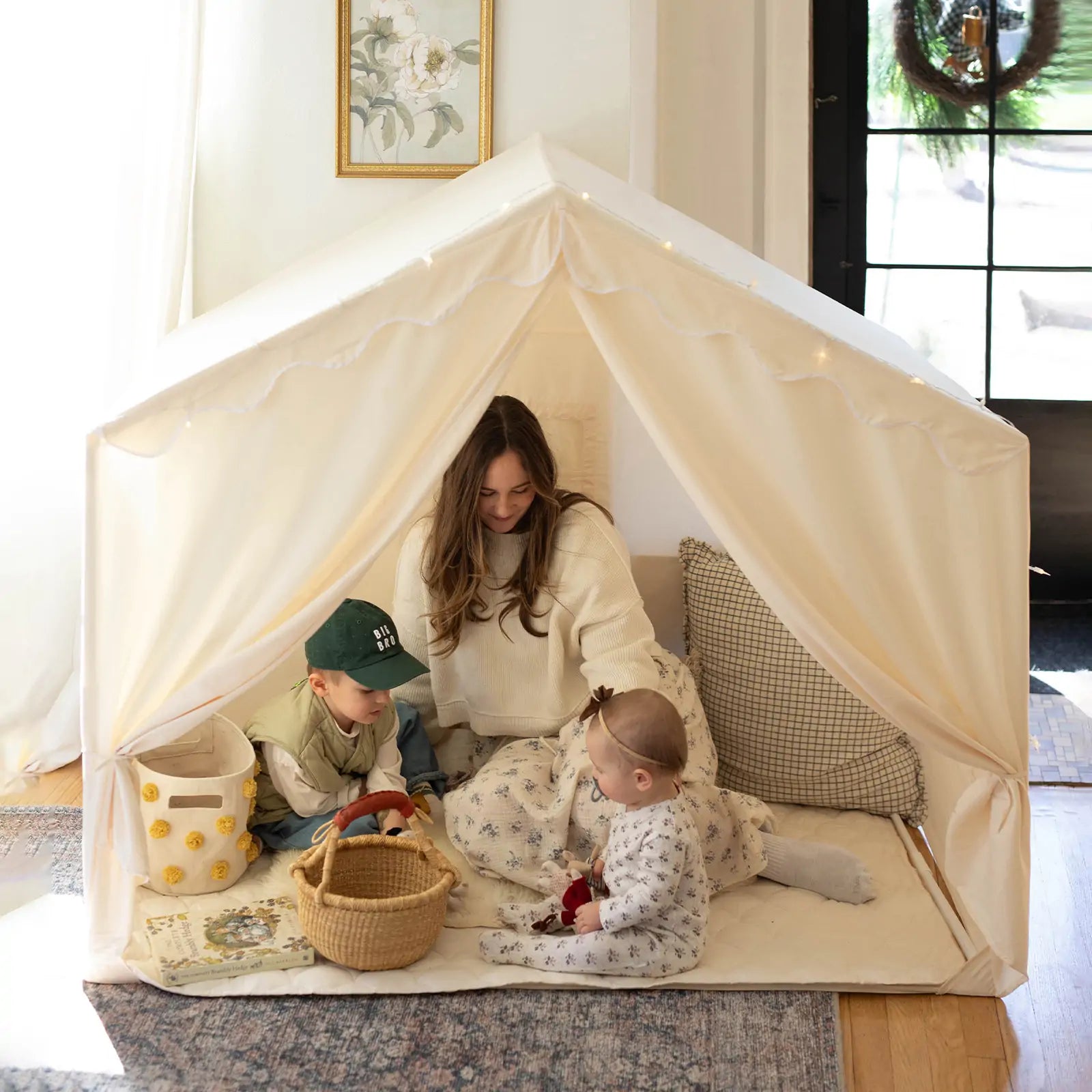 A woman and two children play with toys on a quilted mat inside the spacious Tiny Land® Kids Tent – Large Cozy Tent with Star Lights, enjoying warm natural light for cozy, inviting playtime.