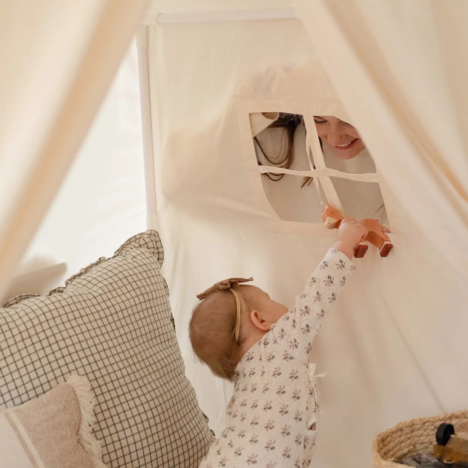 A baby reaches through the Tiny Land® Kids Tent – Large Cozy Tent with Star Lights to hand a toy to a smiling adult, with cozy pillows and a quilted play mat from Tiny Land visible inside.