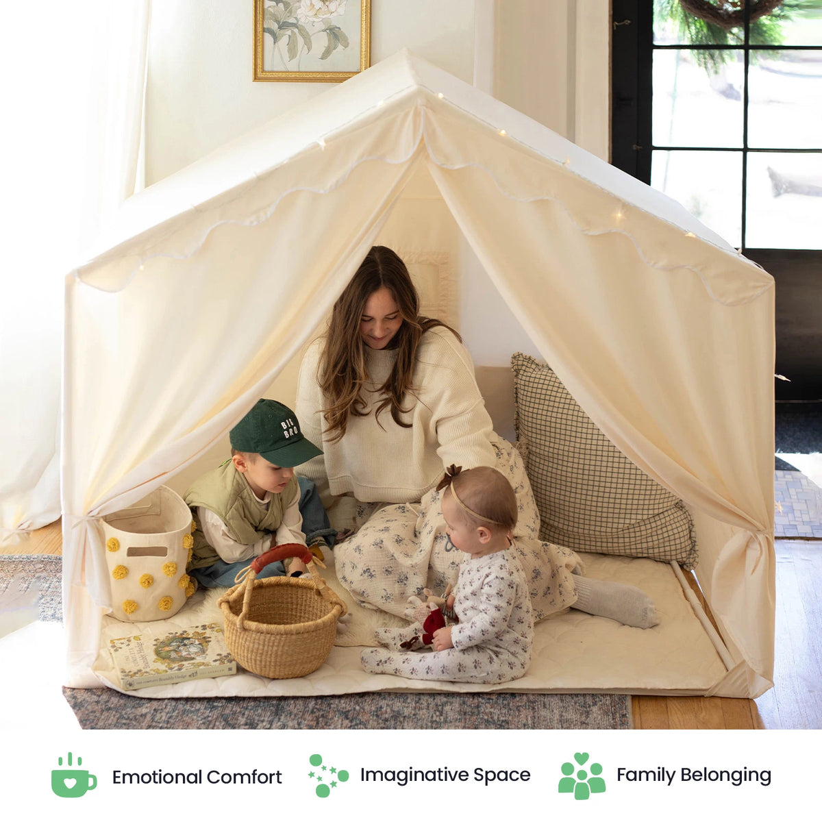 A woman and two young children enjoy quality time together inside the Tiny Land® Kids Tent – Large Cozy Tent with Star Lights, surrounded by soft pillows and baskets in a warmly lit room. Icons below celebrate comfort, imagination, and family belonging—key features of Tiny Land.|fabric