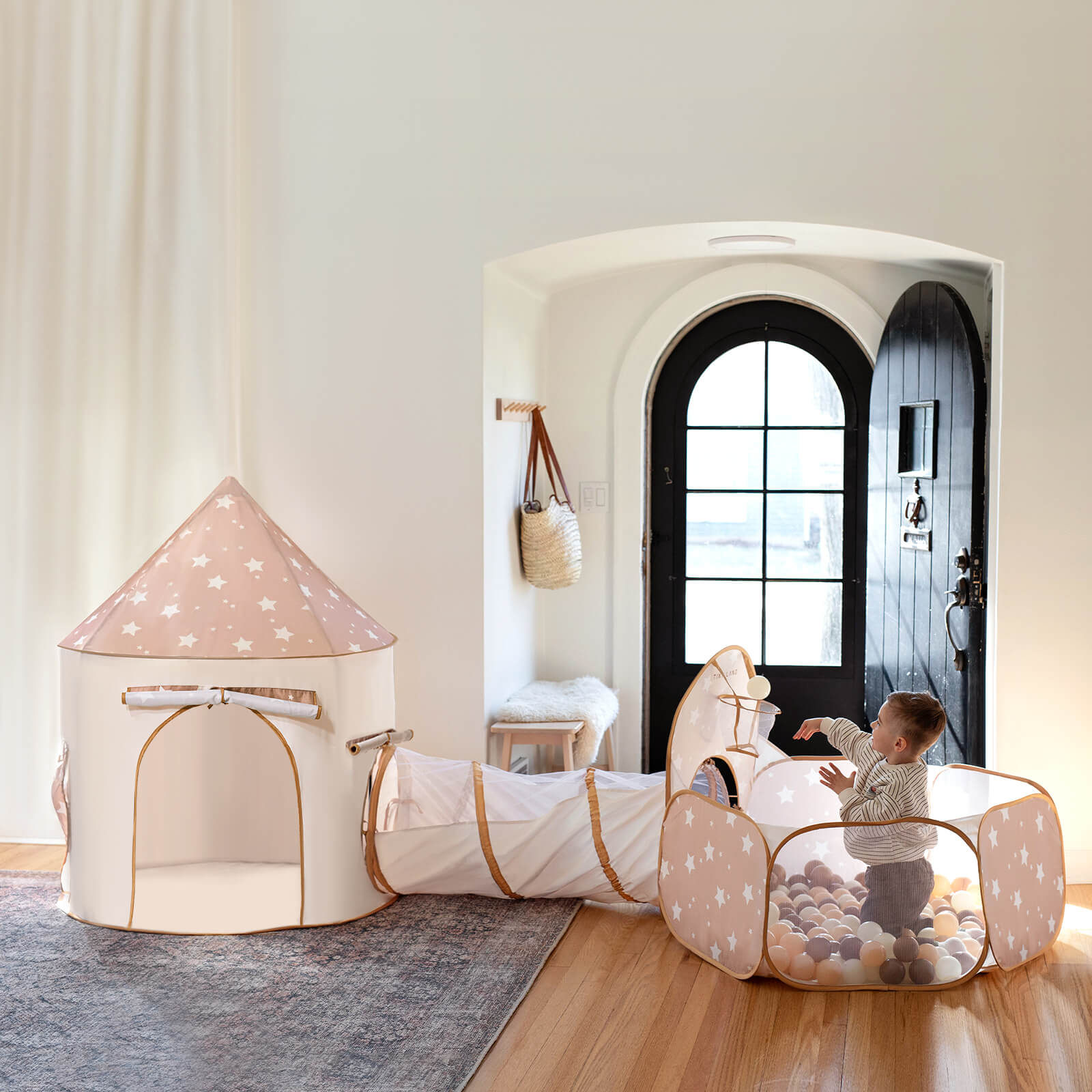A toddler enjoys the Tiny Land® Adventure 3-in-1 Play Tunnel & Ocean Ball Set, featuring a star-patterned ball pit linked to a matching tunnel and tent, all by Tiny Land in a cozy room with playful decor.