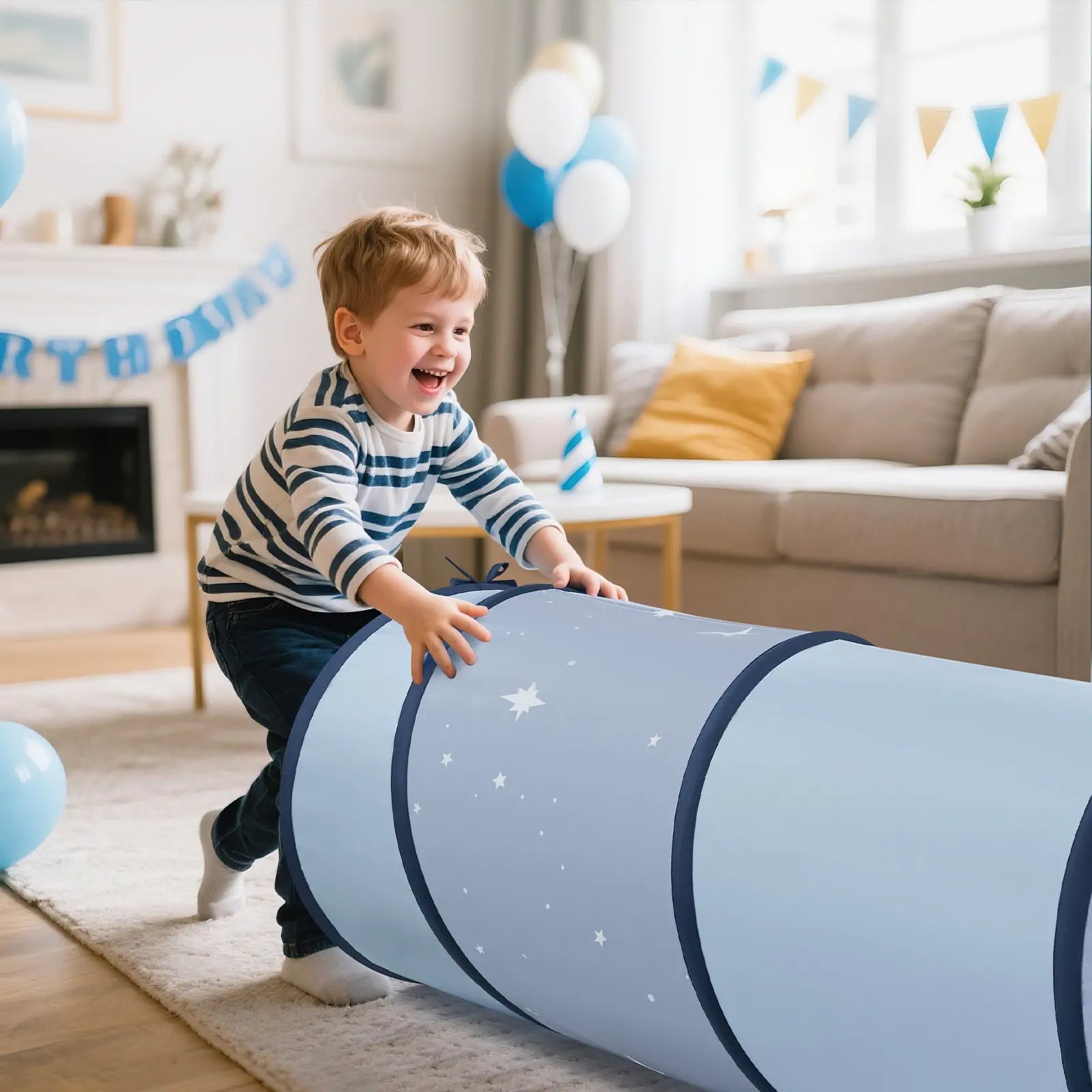 A smiling young boy in a striped shirt pushes the Tiny Land® Adventure Play Tunnel - Blue by Tiny Land, decorated with stars, in a bright living room filled with blue birthday balloons and banners.