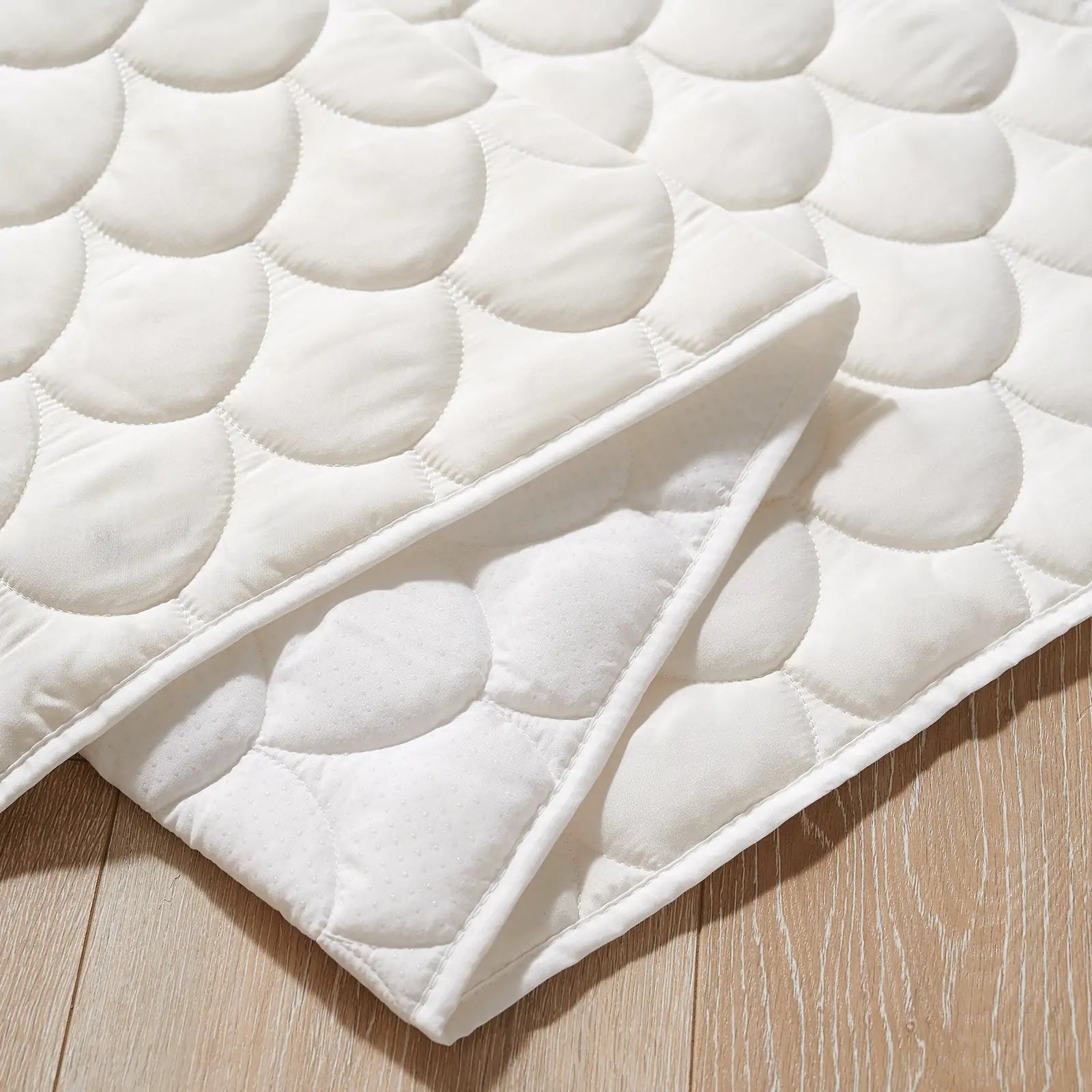 A close-up of a white quilted mat with a circular pattern, folded on a light wooden floor—an ideal padded base for the Tiny Land® Playhouse Tent by Tiny Land, or for use as bedding or a mattress protector in your child’s play space.