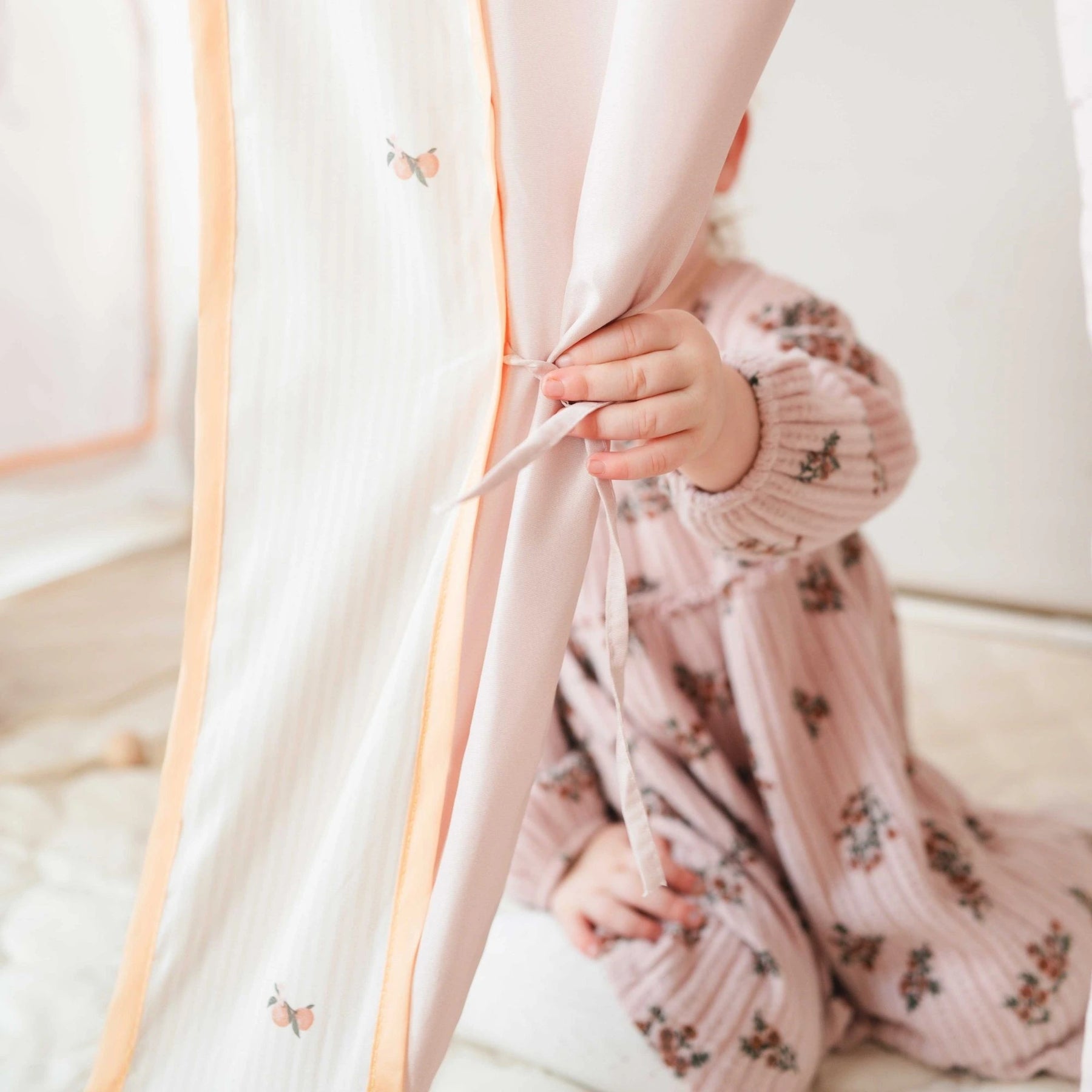 A young child, face hidden, playfully ties a soft curtain on the Tiny Land® Sweet Citrus Kids Play Tent – White and Pink Indoor Playhouse, creating a cozy indoor hideout that inspires imaginative play.