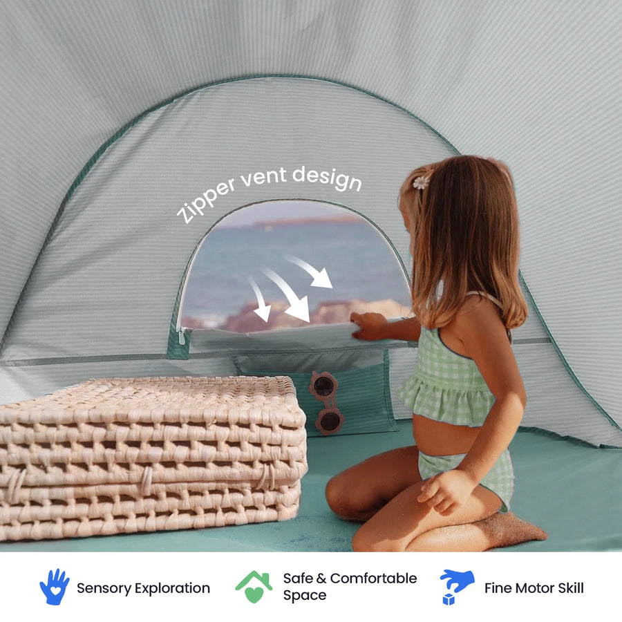 A young girl in a swimsuit sits inside the Tiny Land® One-Stop Beach Toy & Tent Set by the ocean, holding a zipper vent on the UV-protected tent. Beside her are woven mats, sunglasses, and her sand play set. Icons below highlight: Sensory Exploration, Safe & Comfortable Space, and Fine Motor Skill.|Sea Blue