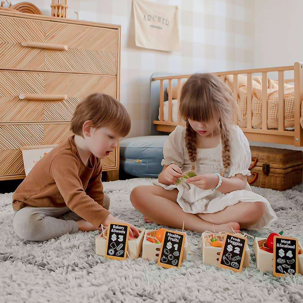 Two young children sit on a soft rug, playing with the Tiny Land® Wooden Food for Play Kitchen & Wooden Rack by Tiny Land, sorting pieces into baskets in a cozy bedroom with a crib and dresser in the background.