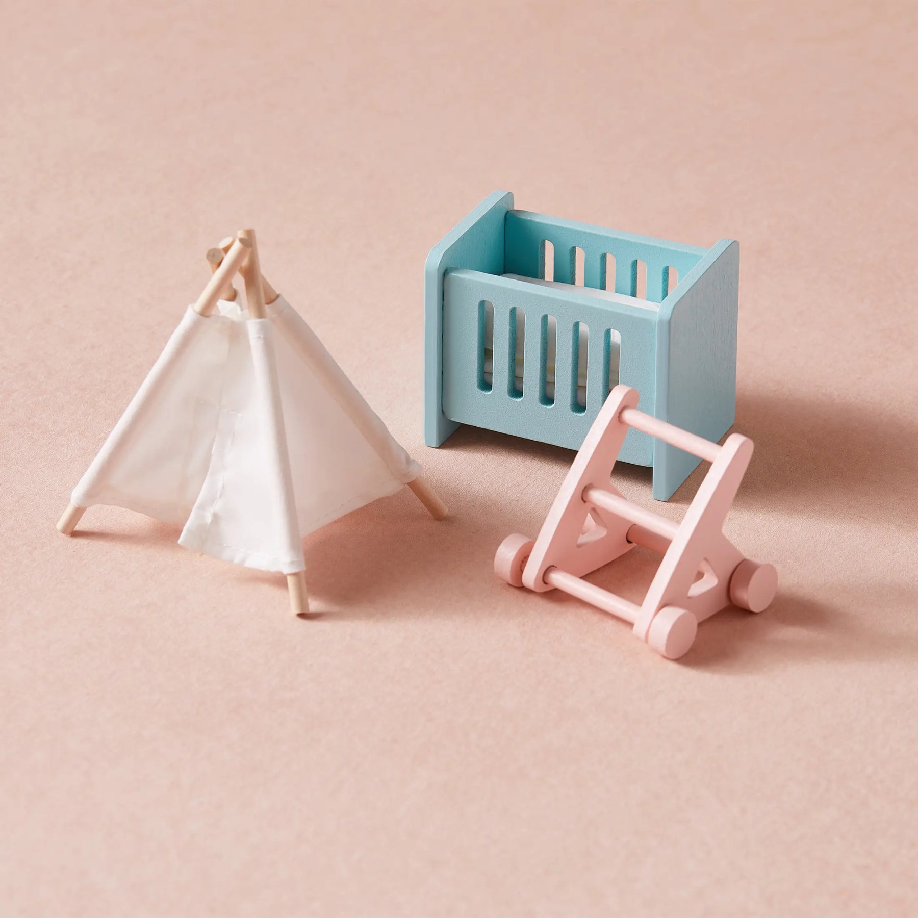 Miniature wooden toys on a pink surface, such as a blue crib, white fabric play tent, and pink baby walker—perfect additions to the Tiny Land® Sweetwood Love Dollhouse without Dolls by Tiny Land for creative play.